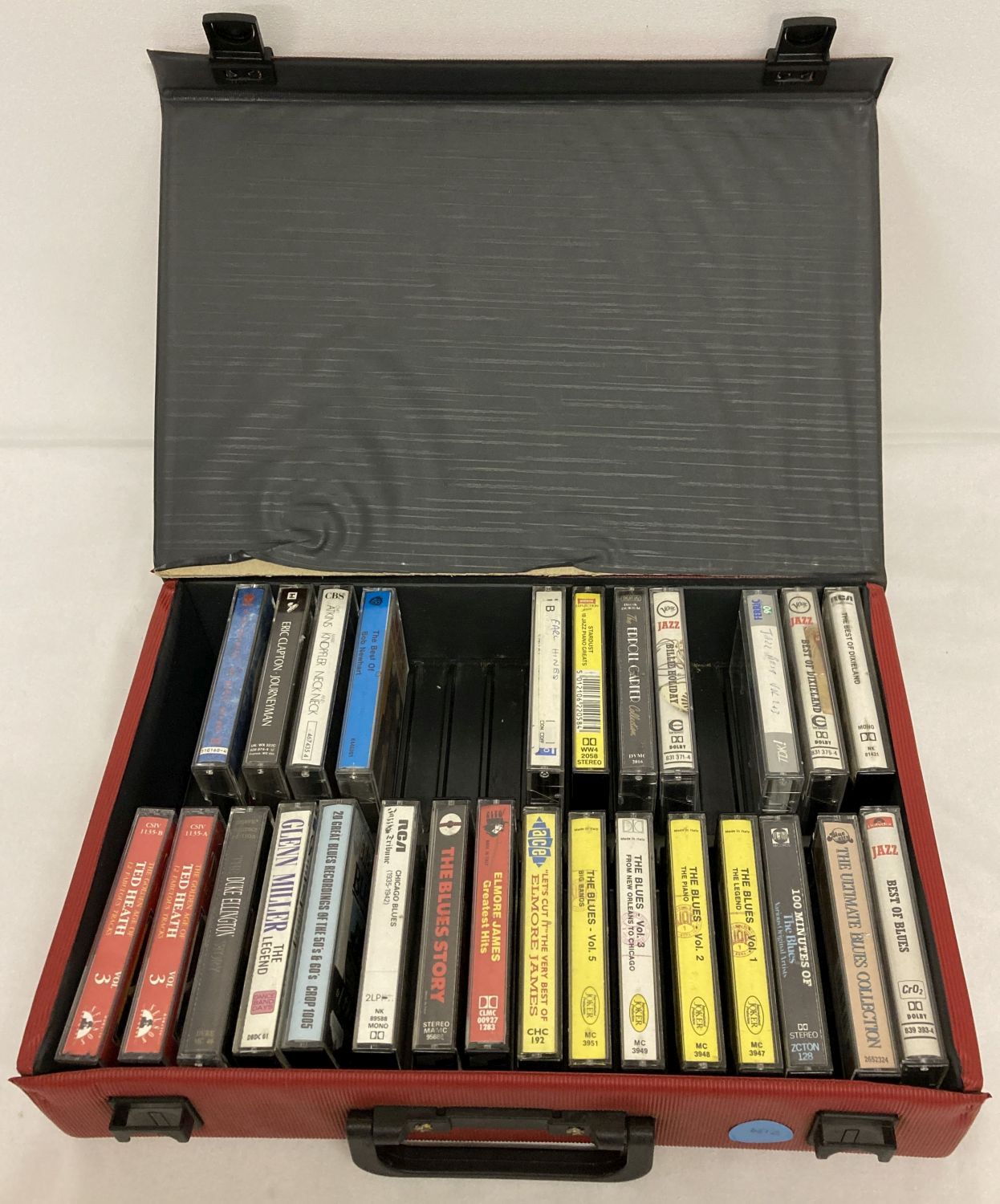 A red case containing a quantity of assorted vintage music audio cassettes.