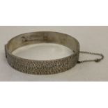 A vintage silver hinged bangle with brushed design detail, complete with safety chain.