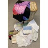 A wicker laundry basket together with a quantity of vintage linen table cloths.