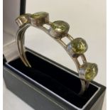 A modern bangle style silver bracelet with 5 large oval cut green stones.