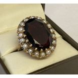 A 9ct gold dress ring set with a large oval cut garnet surrounded by 18 seed pearls.