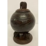 A vintage carved coconut shell canister raised on wooden tripod base with elephant feet.