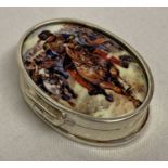 A small oval shaped pill box with ceramic plaque set to lid depicting charging cavalrymen.