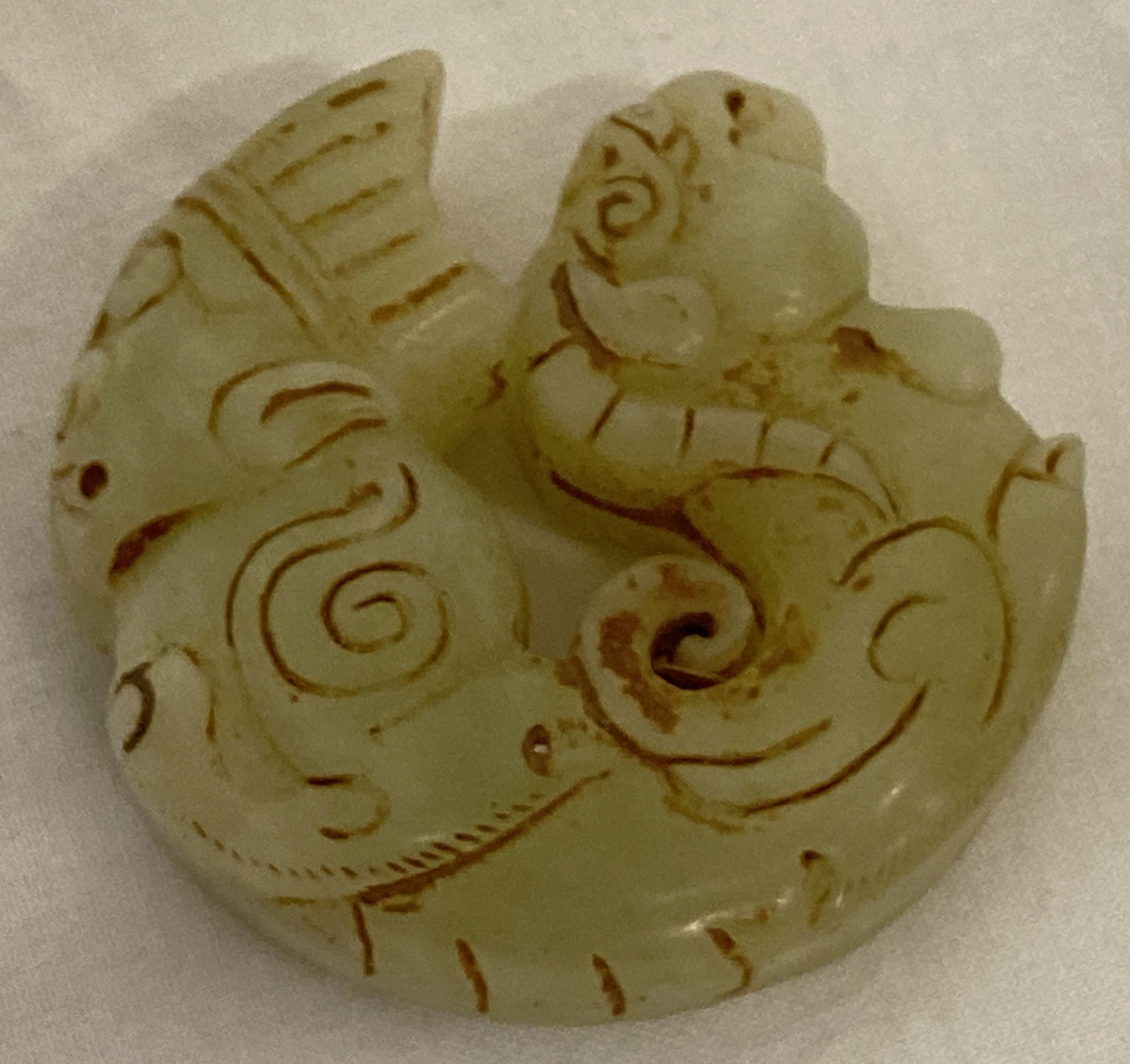 A Chinese Jade roundel depicting figural detail to one end and mythical creature to the other.