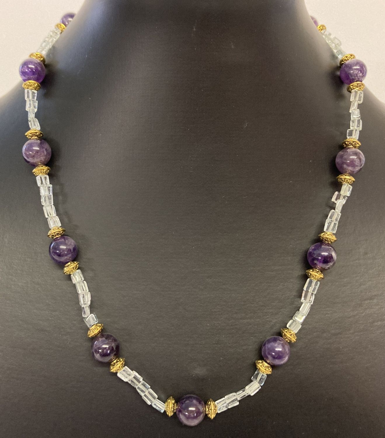 A 17" amethyst and aquamarine beaded necklace with gold tone S shaped hook clasp and spacer beads.