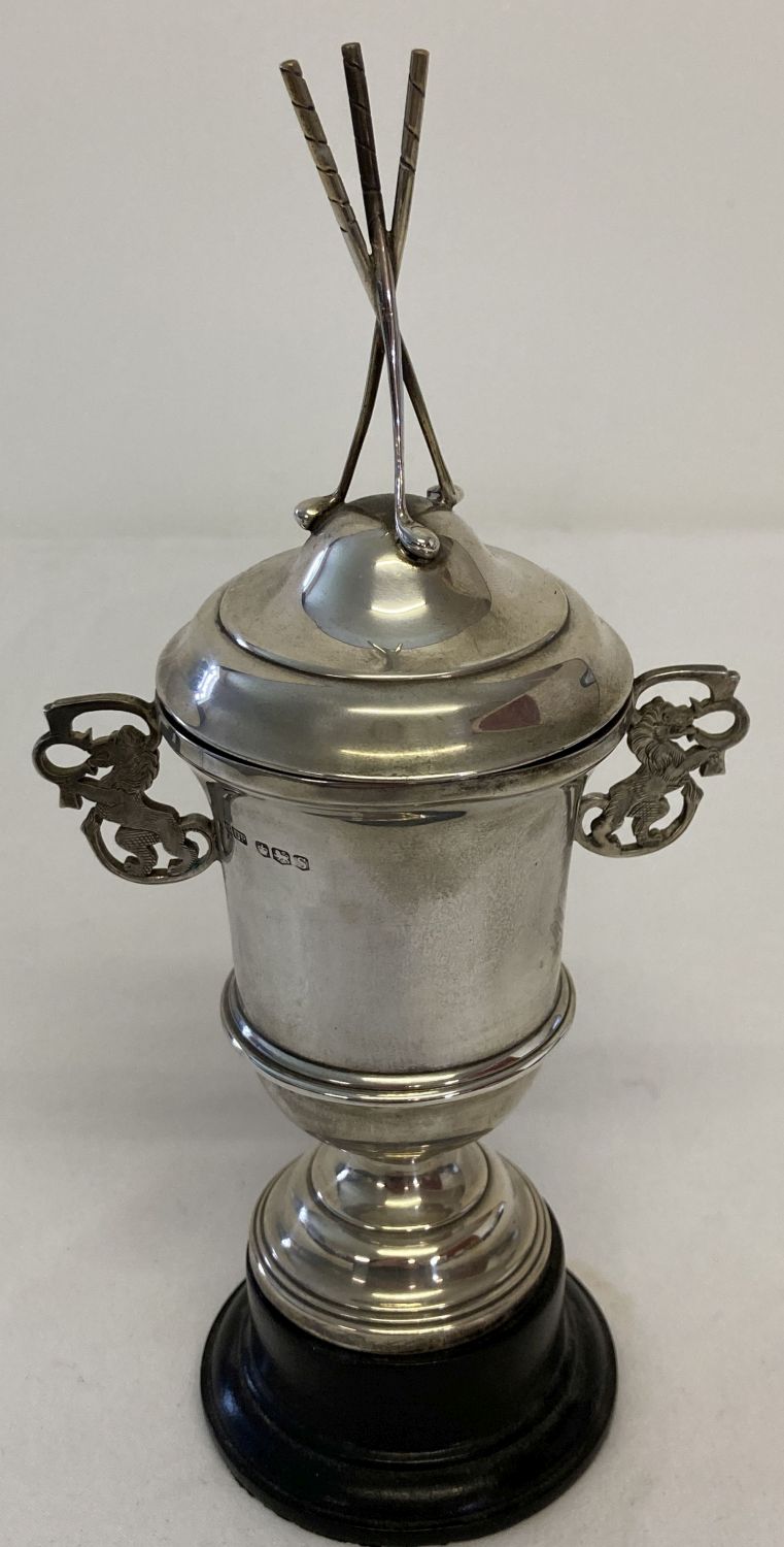 A vintage silver lidded trophy cup with 3 golf club finial to top and pierced work lion handles.