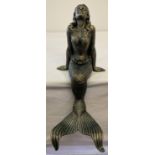 A large cast metal figurine of a mermaid in a seated position.