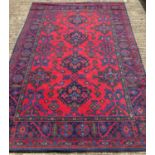 A large vintage wool rug in traditional design. Red ground with blue, green, orange & teal colours.
