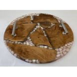 A modern circular tray made from wood, pebbles and clear resin, with chrome handles.