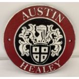 A circular shaped cast iron Austin Healey wall plaque, painted red, black and white.