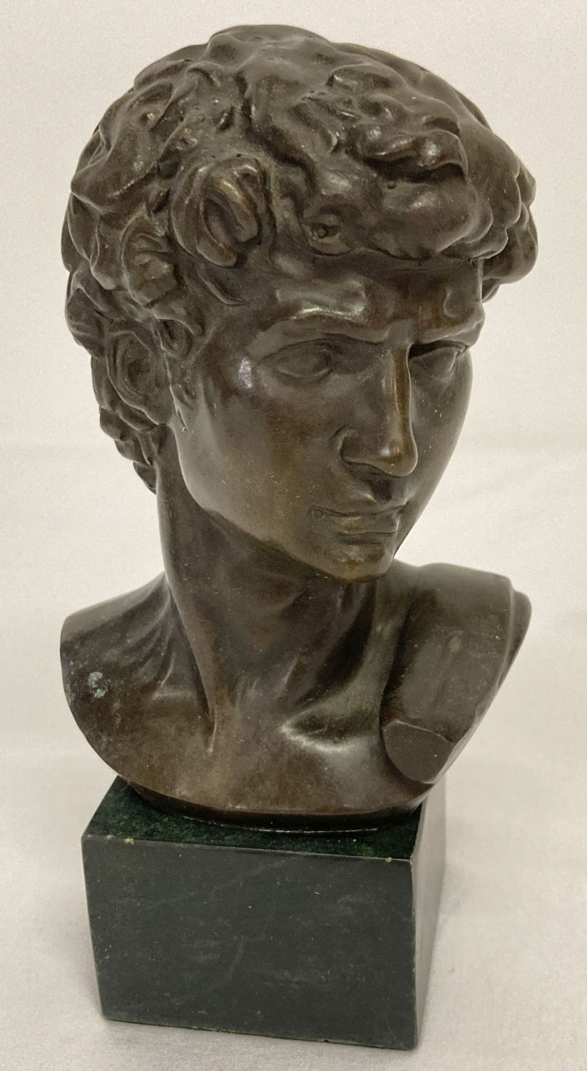 A small bronze bust of David mounted on a square shaped marble base.