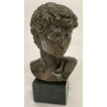 A small bronze bust of David mounted on a square shaped marble base.