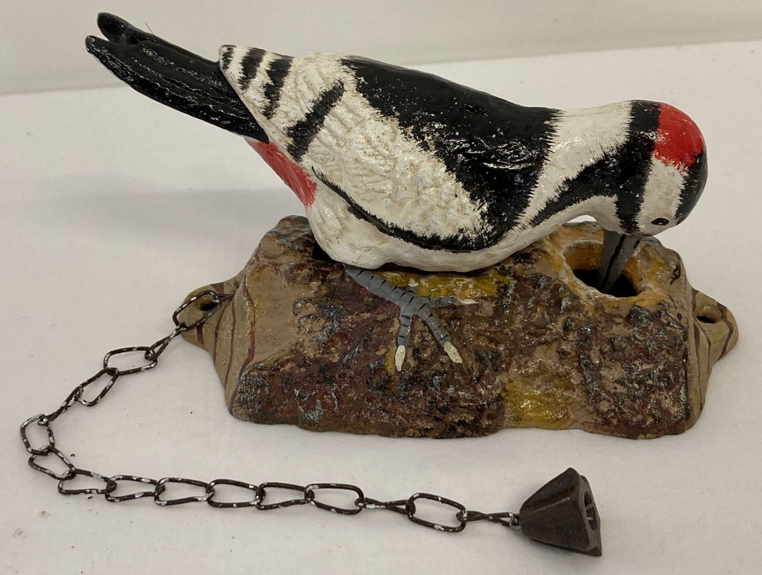 A painted cast metal door knocker in the shape of a woodpecker with fixing holes.