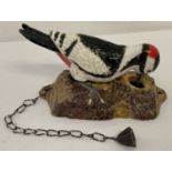 A painted cast metal door knocker in the shape of a woodpecker with fixing holes.