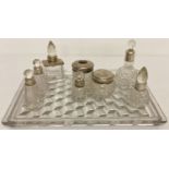 A moulded glass vanity tray with a collection of silver collared perfume bottles and vanity jars.