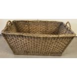 A large vintage wicker laundry basket with carry handles.