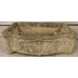 A stone trough style garden planter with carved cherubs and floral detail to front.
