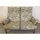 An Ercol light wood framed 2 seater sofa with floral and hummingbird design upholstered cushions.