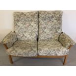 An Ercol light wood framed 2 seater sofa with floral and hummingbird design upholstered cushions.