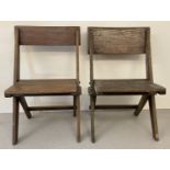 A pair of dark oak Arts & Crafts folding chairs with solid wood seats and x shaped frame.