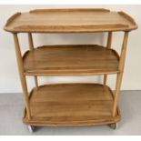 A vintage Ercol light elm 3 tier drinks trolley, on castor feet, with galleried shelves.