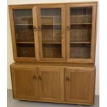 A vintage light elm Ercol 2 sectional triple display unit with twist lock handles and castor feet.