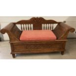A large carved hardwood storage seat with scroll shaped arms, spindle detail and carved back.