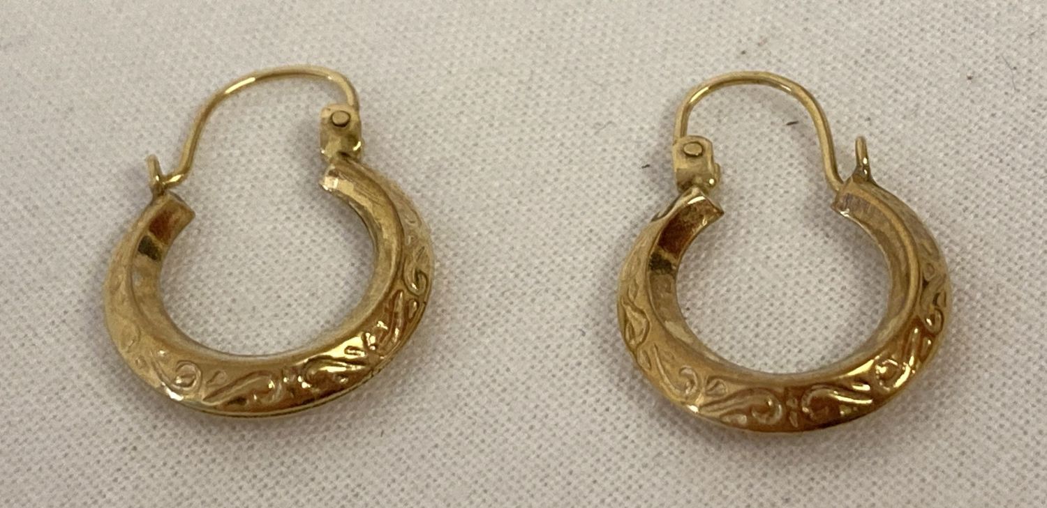 A small pair of creole style gold earrings with floral decoration.