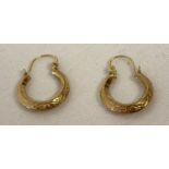 A small pair of creole style gold earrings with floral decoration.