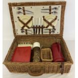 A large vintage wicker picnic basket complete with cutlery, plates and cups.