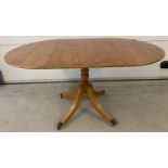 A modern reproduction satin wood veneer drop leaf table with pedestal base.