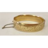 A vintage 9ct gold with metal core hinged bangle with half floral decoration and safety chain.