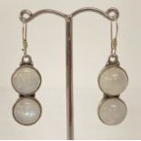 A pair of modern design silver drop earrings set with round cabochon moonstones.