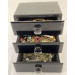 A modern black glass 3 drawer jewellery box containing various costume jewellery.