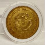 A gold coloured Chinese coin in clear plastic case.