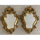 A pair of decorative gilt plaster framed wall hanging mirrors with scroll detail.