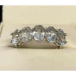 A modern deign silver half eternity style ring set with 6 oval cut blue topaz stones.