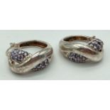 A pair of modern twist design hoop earrings set with lilac coloured stones. each earring marked '