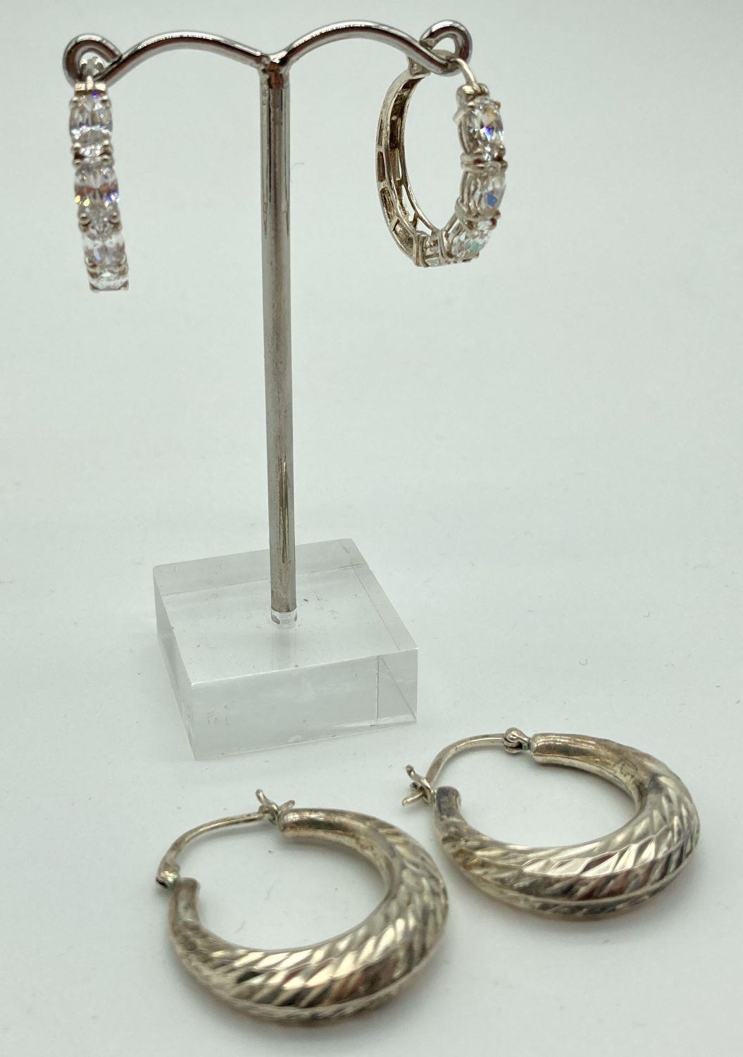2 pairs of silver hoop style earrings. One pair with a diamond cut design the other set with oval