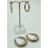 2 pairs of silver hoop style earrings. One pair with a diamond cut design the other set with oval