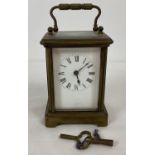 A small antique brass and glass panel carriage clock with white enamel face. Complete with key.