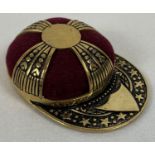 A gilt novelty pin cushion in the shape of a jockey's hat, with burgundy coloured velvet cushion.
