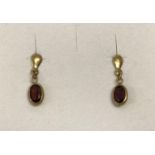 A small pair of 9ct gold and garnet set drop style earrings. Each earring set with an oval cut