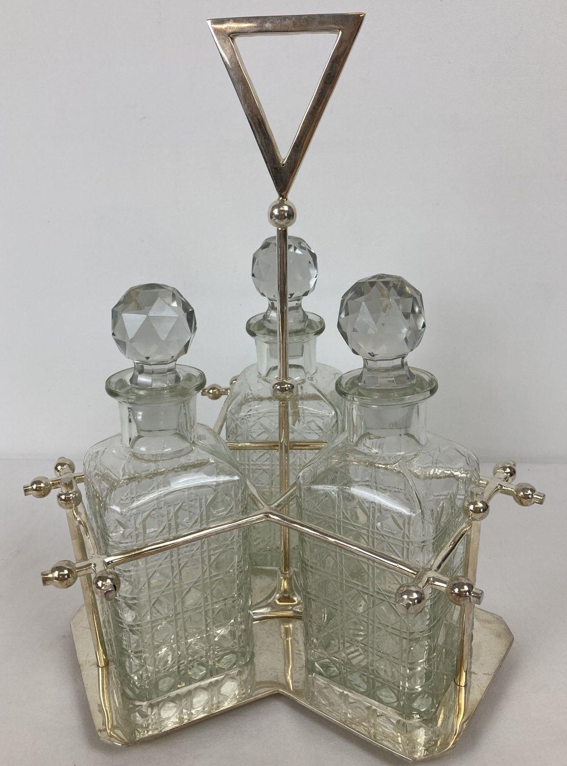 A silver plated triple decanter stand tantalus with 3 cut glass decanters. Central screw in stem