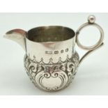 A small Victorian silver cream jug decorated with scrolls and waves of foliage. Loop design handle