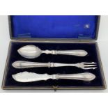 A cased silver plate condiment cutlery set. Comprising: jam spoon, pickle fork and cheese/fruit