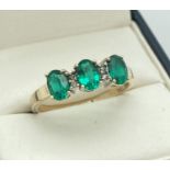A 9ct gold diamond and created emerald dress ring. 3 oval cut emeralds in a trilogy setting, with
