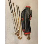 A black and red vintage golf club bag with a collection of vintage golf clubs in varying sizes and