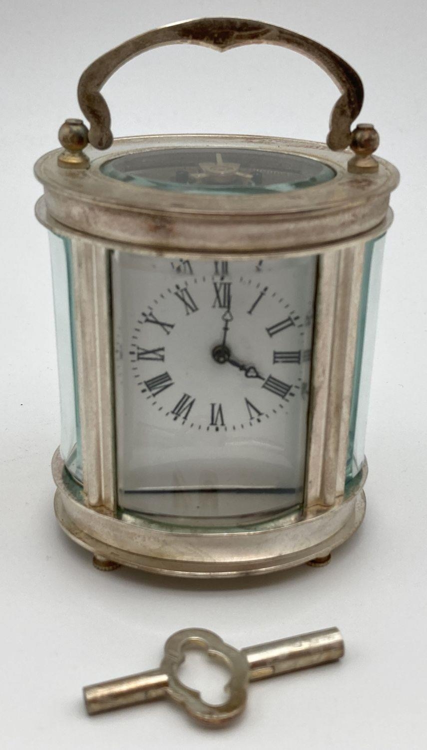 A small oval shaped carriage clock with glass panelled sides and top, enamelled face and roman