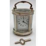 A small oval shaped carriage clock with glass panelled sides and top, enamelled face and roman